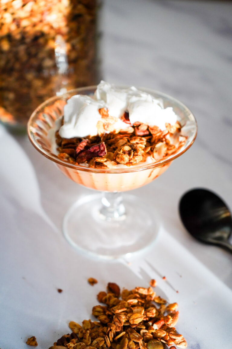 a dessert dish of homemade pumpkin pecan granola with greek yogurt ready to eat, granola sprinkled on marble counter.