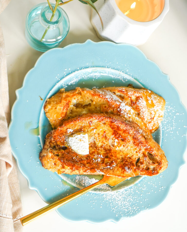 a blue plate on a white table with homemade french toast, topped with maple syrup and butter.