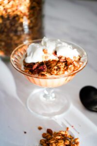 A dessert dish with pumpkin maple pecan granola and greek yogurt on a marble counter