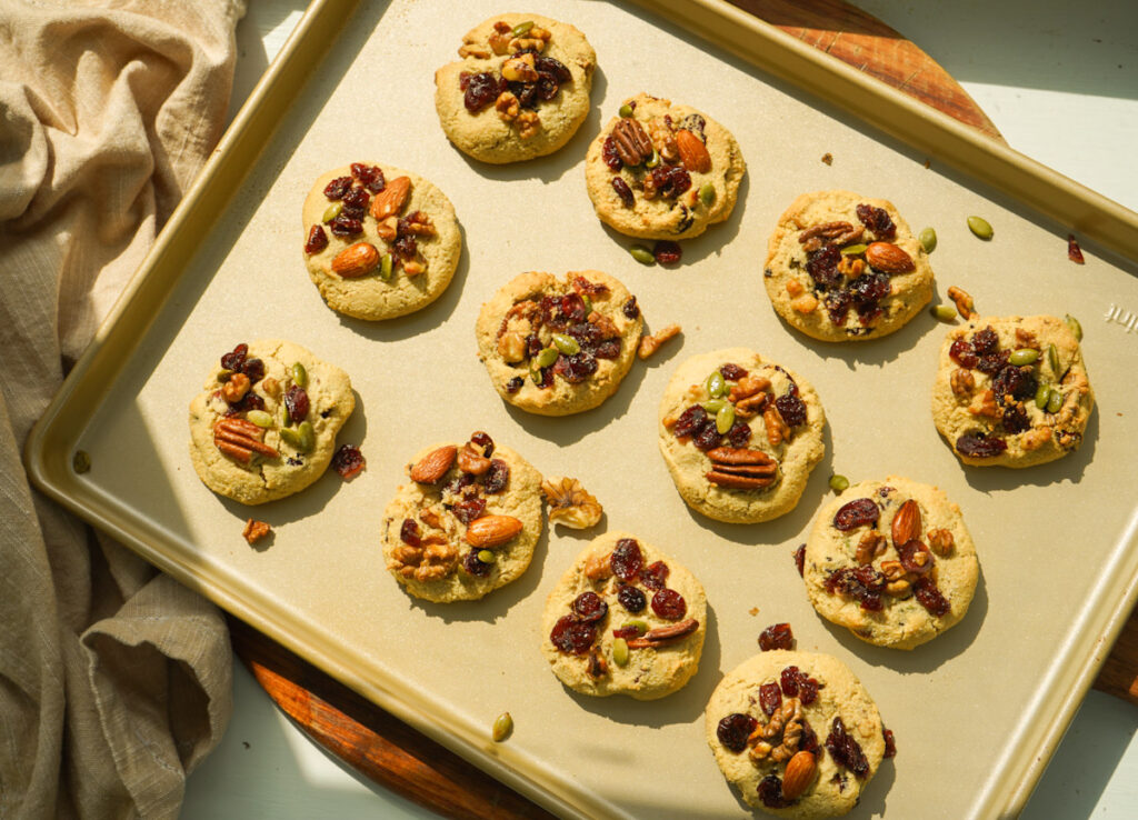 A gold baking tray showing 12 freshly baked almond flour trail mix cookies.