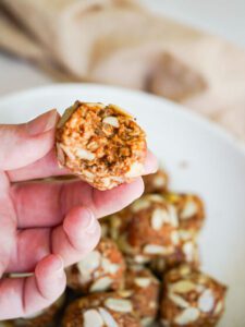 hand holding finished almond energy bite over a plate of finished almond energy balls