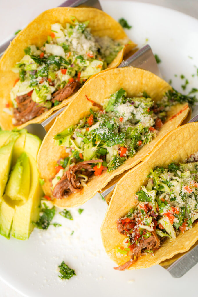 three chipotle beef tacos with cabbage slaw on a white plate ready to eat