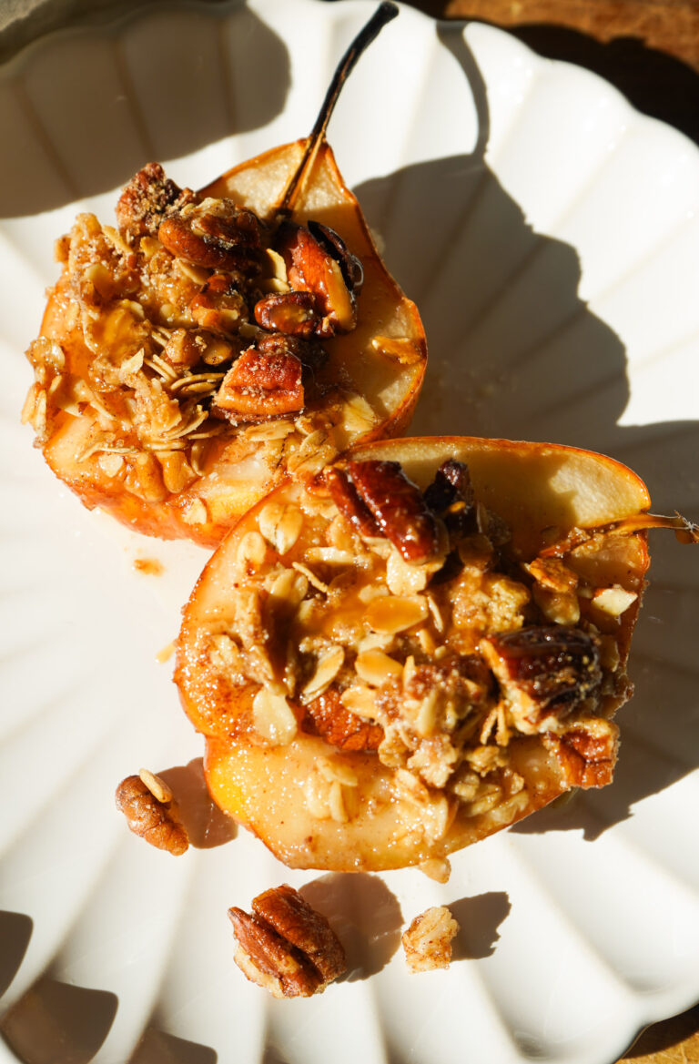 two baked pear halves filled with cinnamon pecan oat crumble on a white scalloped plate in golden sunlight