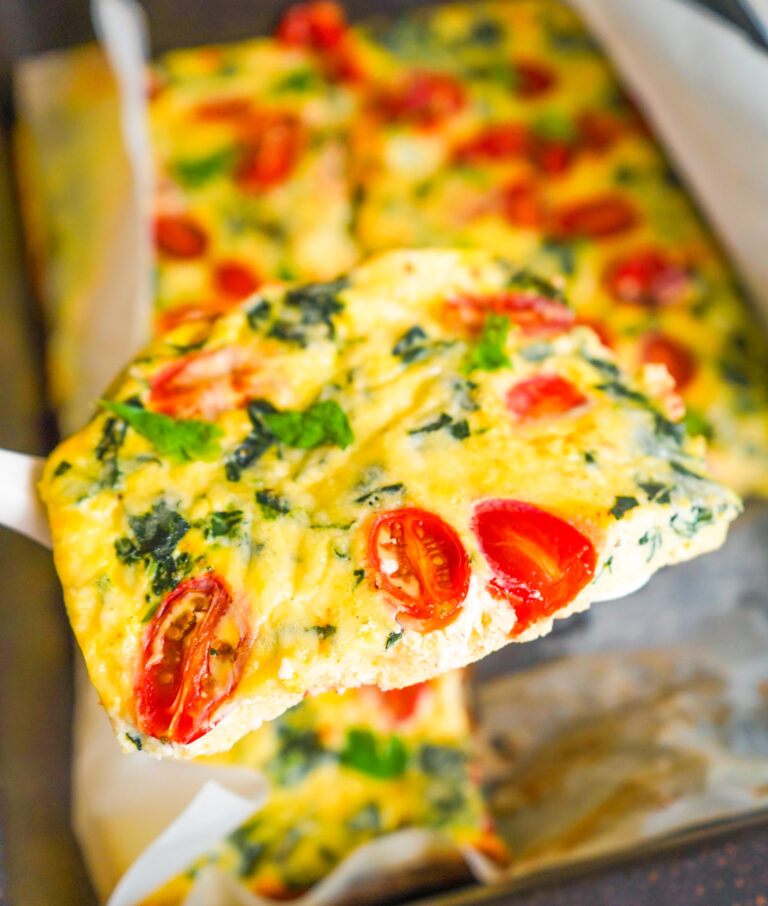 Spatula holding up a slice of protein egg bake with tomatoes and spinach and cheddar.