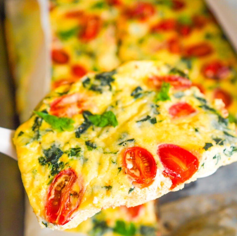 Spatula holding up a slice of protein egg bake with tomatoes and spinach and cheddar.