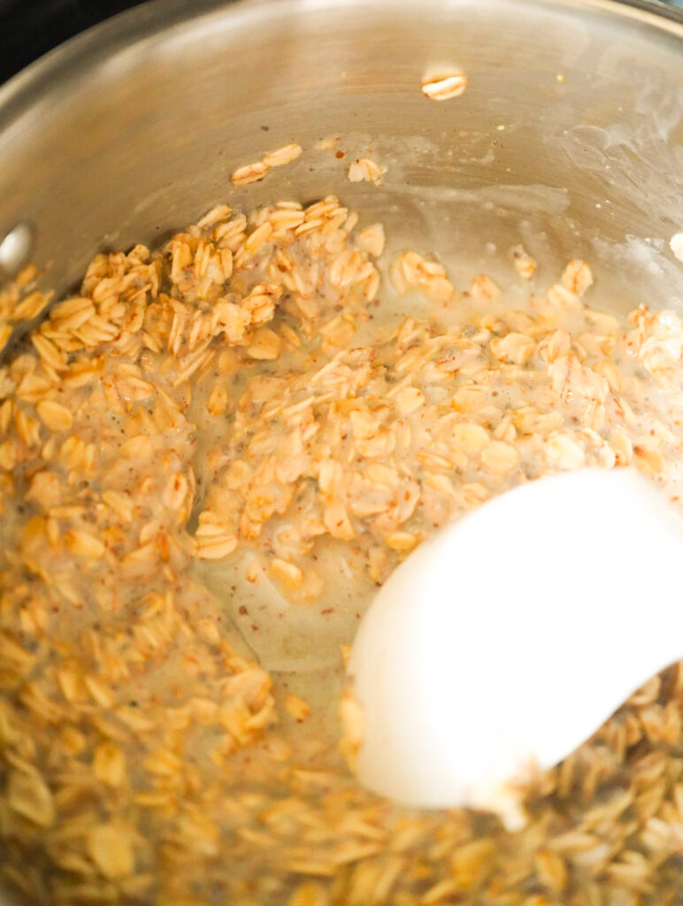 large white spoon mixing oatmeal cooking on the stovetop.