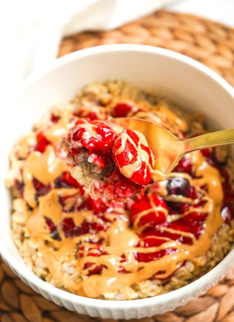 a white fluted bowl with PB & J Oatmeal in it, a gold spoon showing the texture, ready to take a bite.