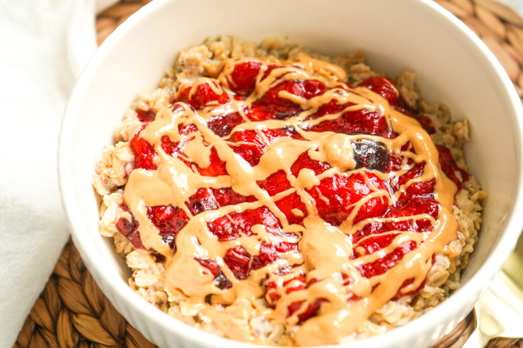 Creamy PB & J oatmeal topped with warm, jammy berries and a peanut butter drizzle in a cozy white bowl.