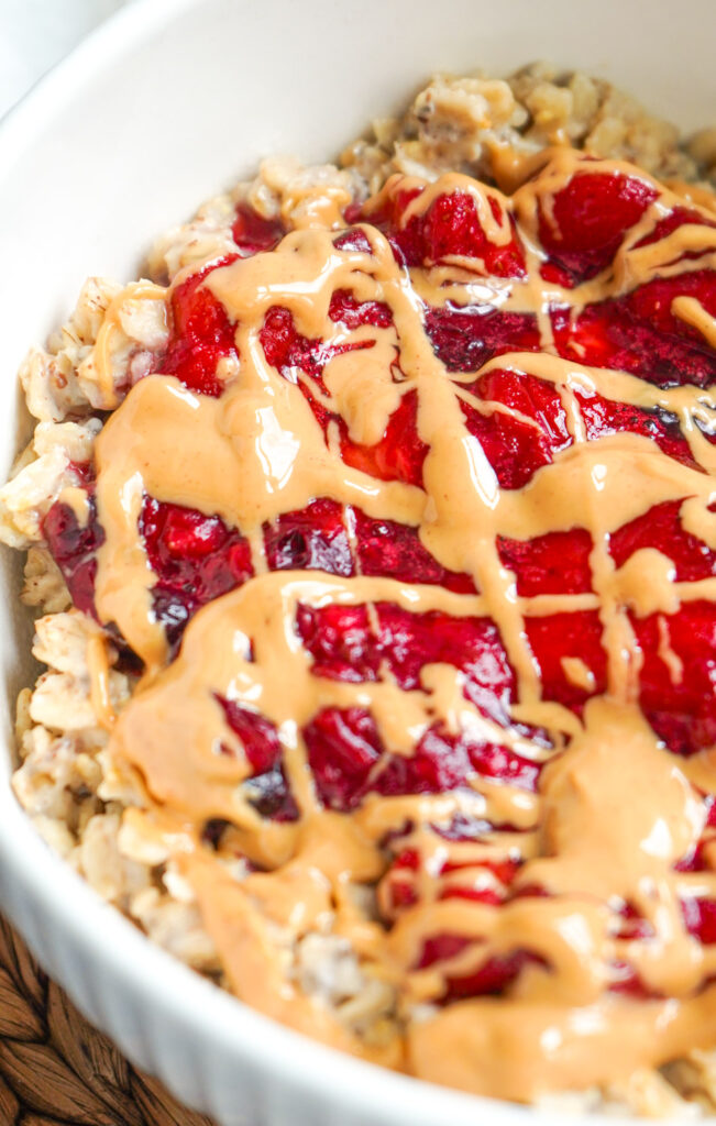 Creamy PB & J oatmeal topped with warm, jammy berries and a peanut butter drizzle in a cozy white bowl.