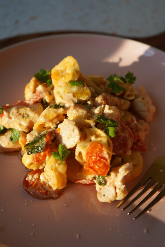 baked chicken tortellini with spinach tomatoes and feta ready to eat on a pink plate in natural light