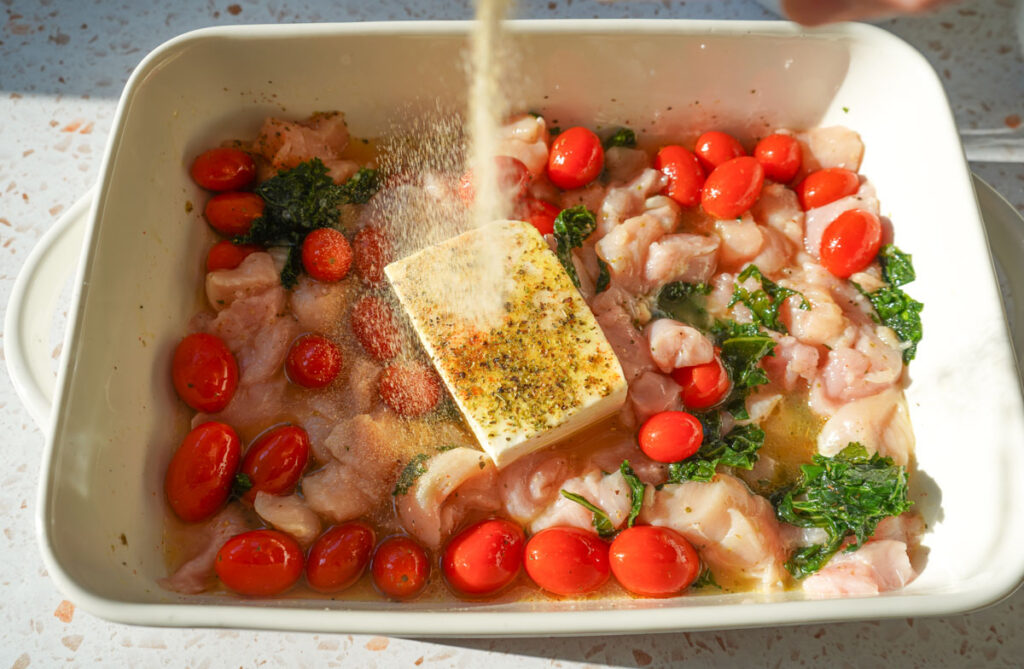 ingredients for chicken tortellini bake in a white casserole dish, seasoning being sprinkled on