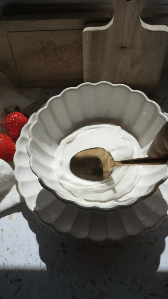 Smoothing out greek yogurt with a gold spoon in a white scalloped bowl.