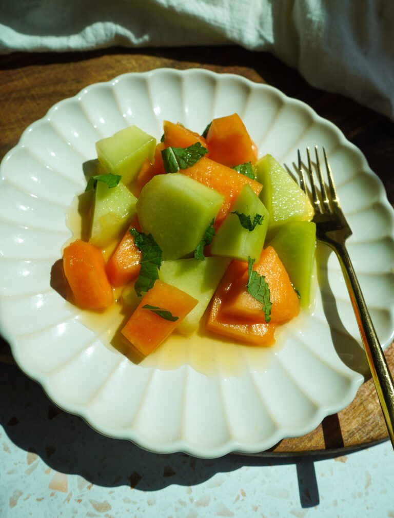 Healthy honeydew and cantaloupe melon salad with honey lime mint dressing served on a large white plate with fresh mint garnish
