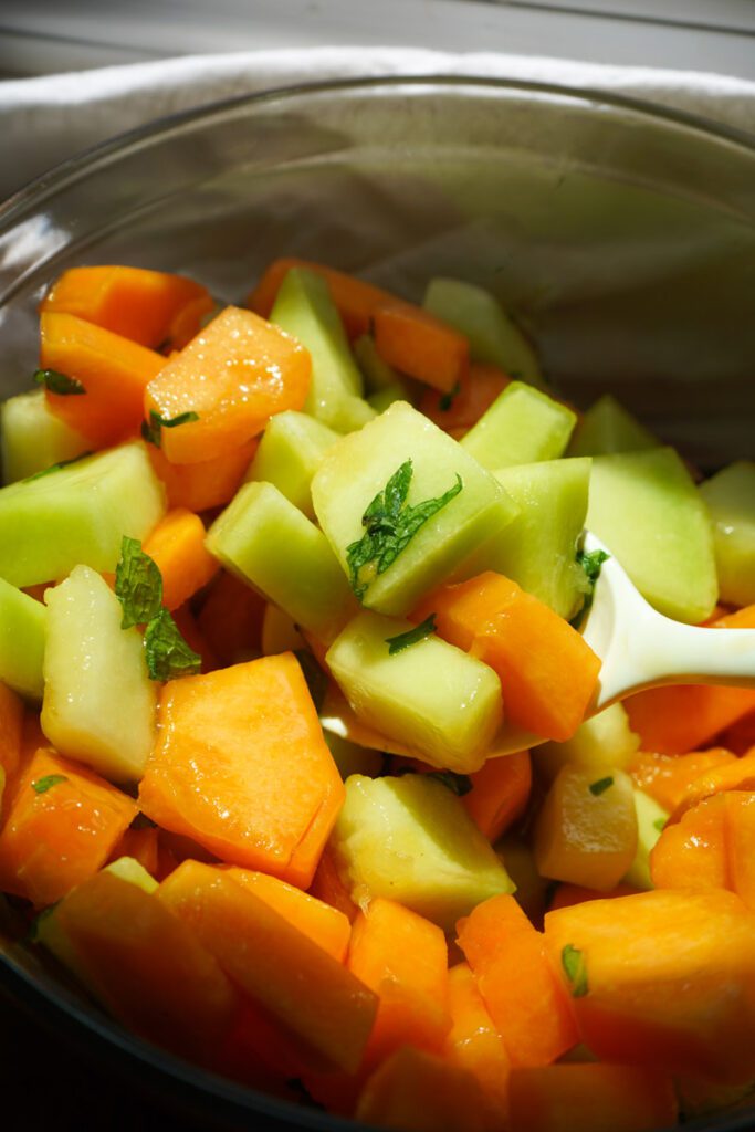 Honeydew & Cantaloupe Melon Salad with Honey Lime Mint Dressing being scooped with a white serving spoon.