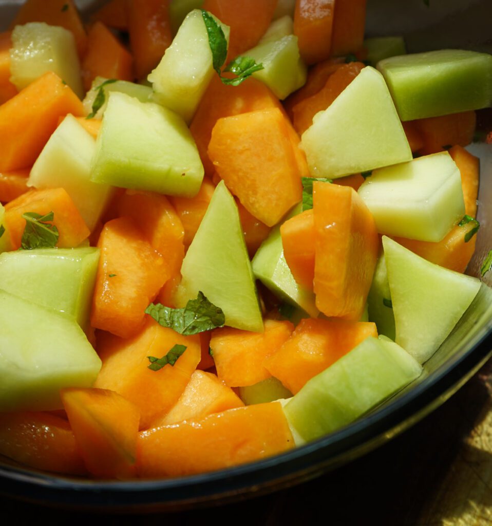 A summer melon salad plated and ready to serve, garnished with fresh mint leaves and a honey drizzle.