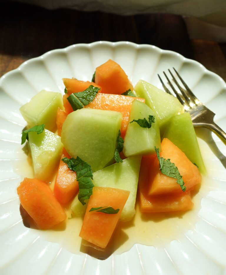A close up detail shot of the melon salad showing the texture of the ripe fruit, fresh mint leaves and glossy honey lime dressing.