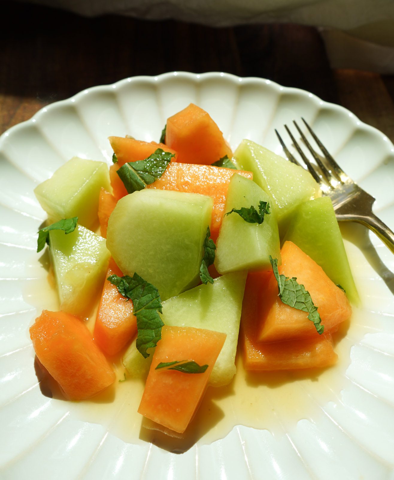 A close up detail shot of the melon salad showing the texture of the ripe fruit, fresh mint leaves and glossy honey lime dressing.