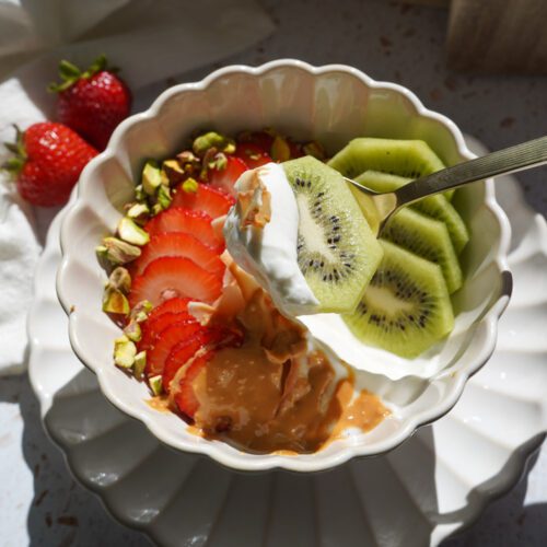 Spoonful of creamy vanilla Greek yogurt and fresh kiwi lifted from a strawberry kiwi yogurt bowl with toasted coconut and pistachios.
