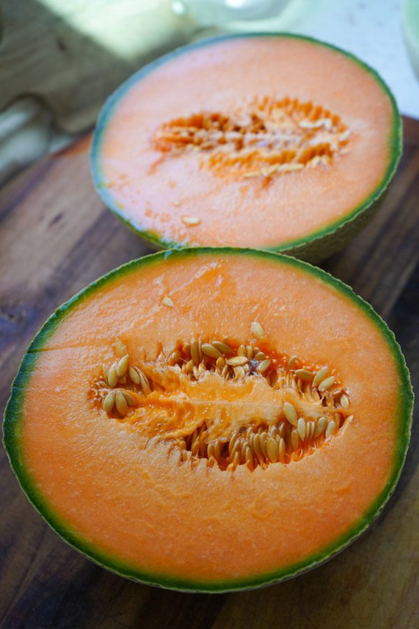 A ripe orange cantaloupe sliced open on a cutting board ready to prepare