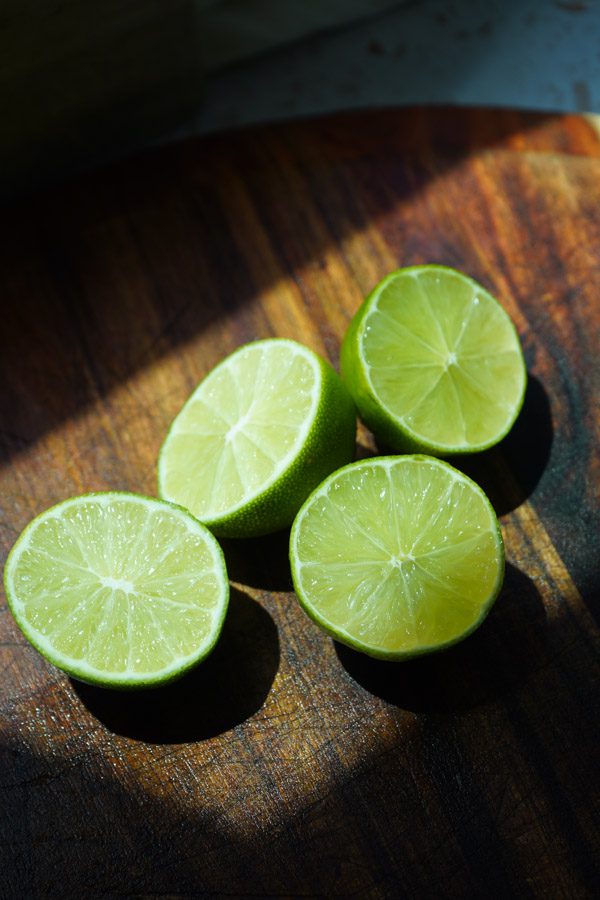 Two limes sliced in half on a brown cutting board in the sunlight