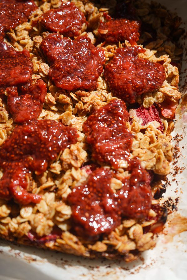 Close up of homemade strawberry chia jam dolloped over golden strawberry chia jam oat squares showing the deep ruby red jam on the crumble top