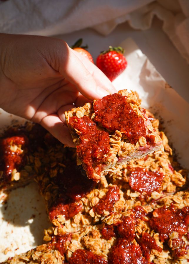 Strawberry chia jam oat squares hand showing golden oat crumble and deep ruby strawberry chia jam on top