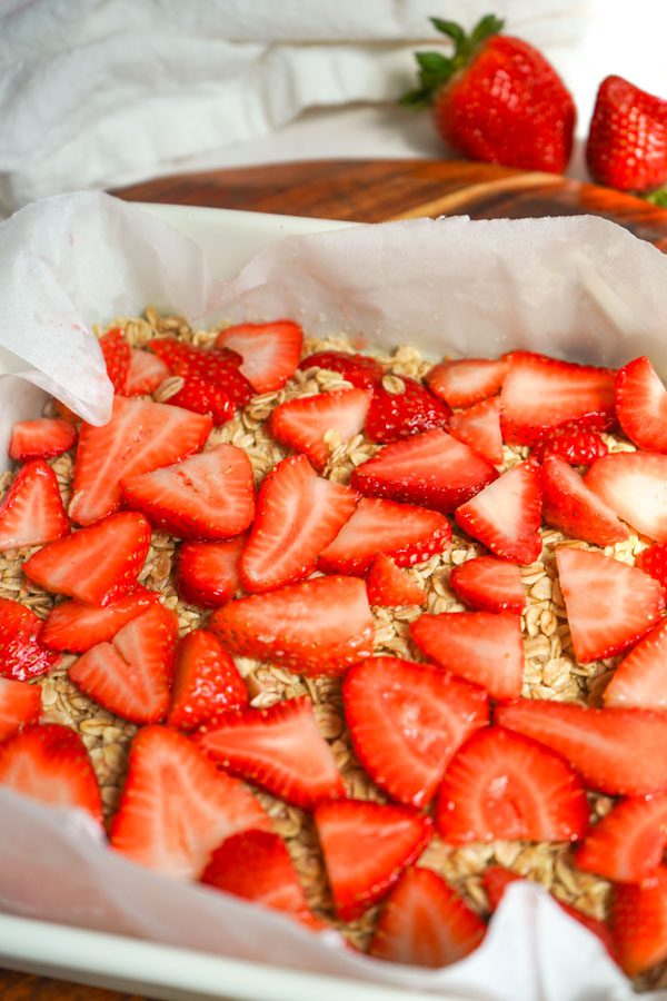 Close up of fresh sliced strawberries layered over a golden oat base in a parchment lined pan before baking