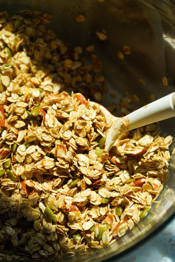 Honey roasted almond granola mixture being stirred in a large bowl before baking.