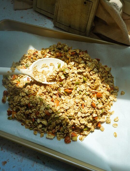 Homemade honey roasted almond granola spread on a parchment-lined baking sheet before baking.