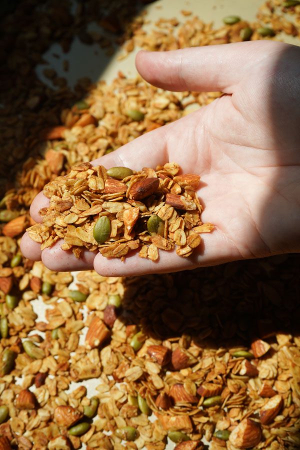 Hand holding a handful of homemade honey roasted almond granola with almonds and pumpkin seeds.