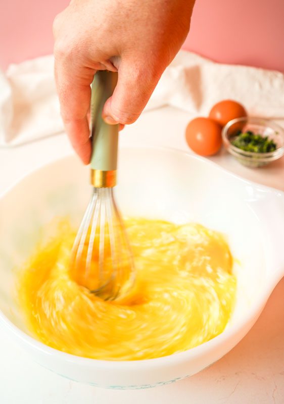 Whisking eggs, yogurt, and Parmesan together in a white bowl to make protein-packed egg and spinach fingers for toddlers.