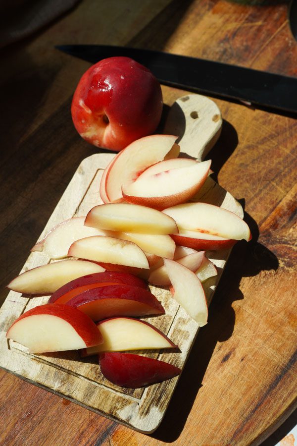 Fresh nectarine sliced into wedges on a small wooden cutting board in warm natural sunlight with a whole nectarine and knife alongside