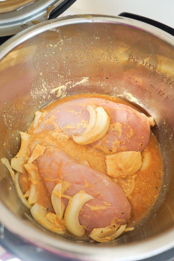 Raw chicken breasts, sliced yellow onions, and apple cider inside an Instant Pot insert ready to be pressure cooked.