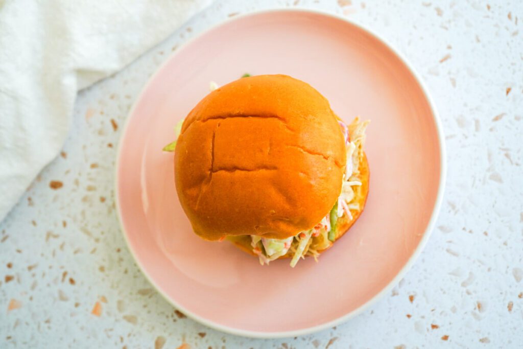 Overhead view of an apple cider pulled chicken sandwich served on a pink plate with a bright, clean background.