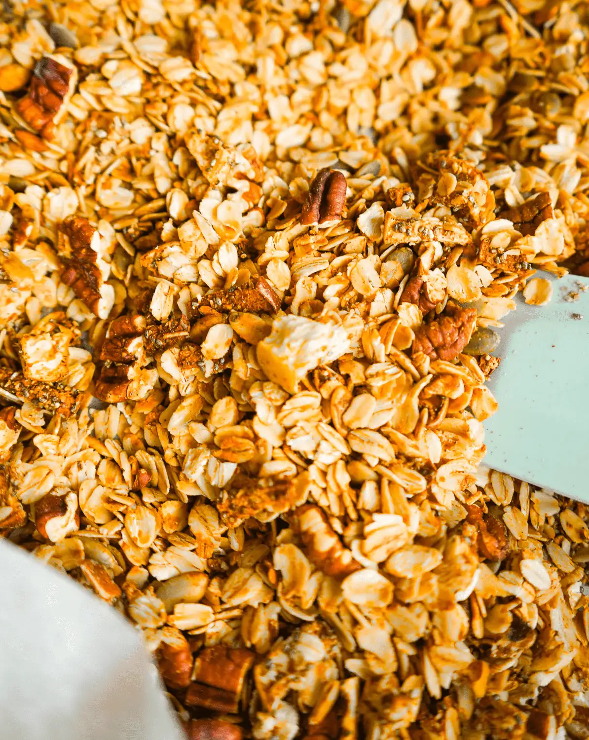 Golden toasted apple cinnamon pecan granola spread across a baking sheet with baked apples and pepitas.