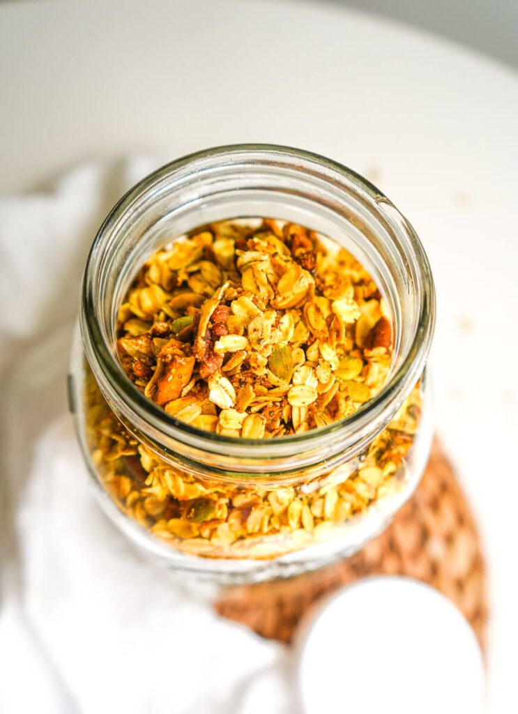 Top-down close-up shot into an open mason jar showing toasted oats, pecans, pepitas, and dried apples.