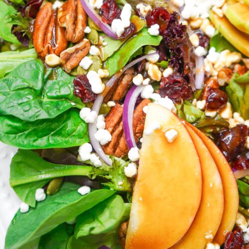 Close-up of an apple pecan salad with maple balsamic vinaigrette glistening on fresh mixed greens.