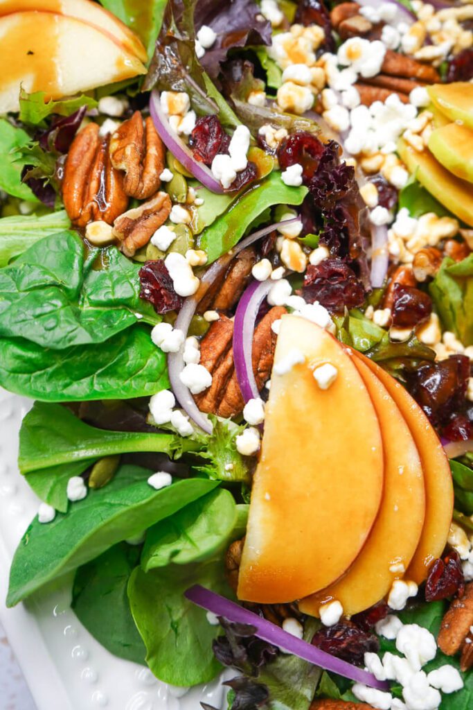 Close-up of an apple pecan salad with maple balsamic vinaigrette glistening on fresh mixed greens.
