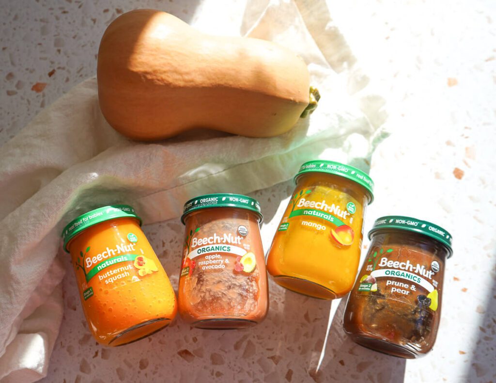 Four jars of Beech-Nut baby food purees sitting next to a raw butternut squash on a countertop.