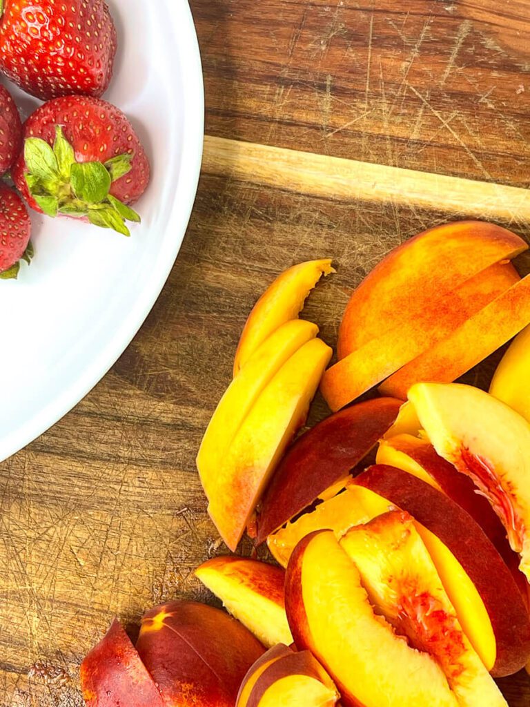 Fresh strawberries and sliced peaches on a wooden cutting board for a healthy baked oatmeal recipe.