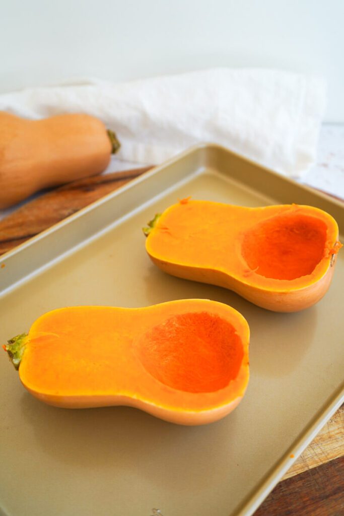 Two butternut squash halves with seeds removed ready to be baked on gold baking tray