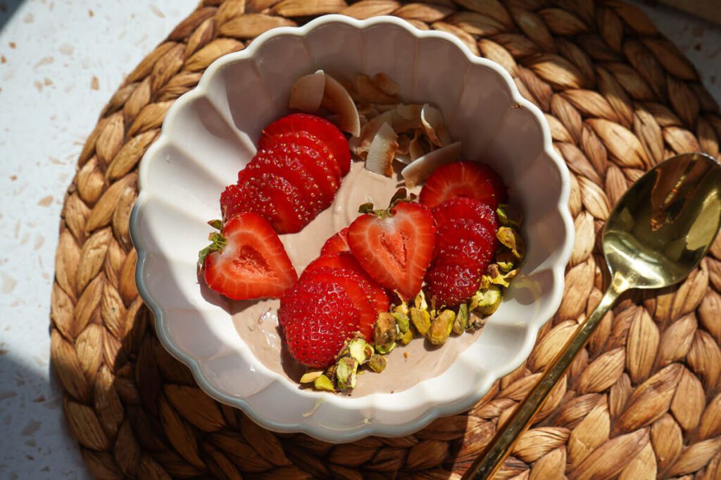 Overhead plated view of high protein chocolate Greek yogurt bowl with sliced strawberries and toasted coconut.