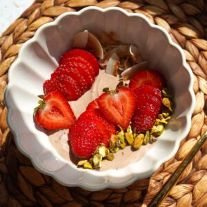 Overhead square view of high protein chocolate Greek yogurt bowl with sliced strawberries and toasted coconut.