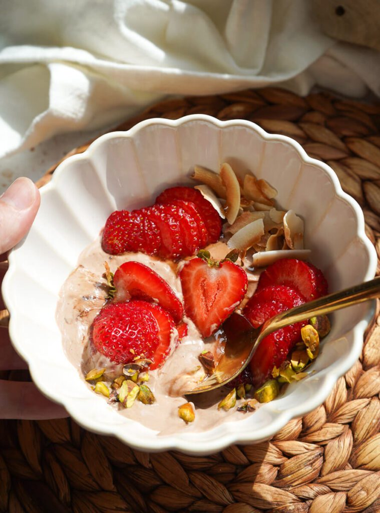 Close up of bowl and spoon scooping velvety chocolate Greek yogurt with fresh strawberry and pistachio.
