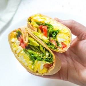 Close-up shot of a toasted egg wrap cut in half showing creamy avocado and melted cheese layers.