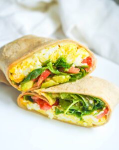 Scrambled egg and avocado breakfast wrap sliced diagonally on a plate for a quick healthy meal.