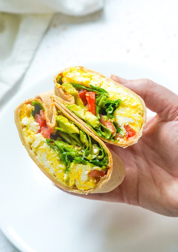 Close-up shot of a toasted egg wrap cut in half showing creamy avocado and melted cheese layers.