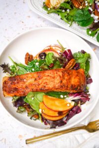 Air fryer maple balsamic salmon fillet served over salad greens on a wide white bowl with gold fork.