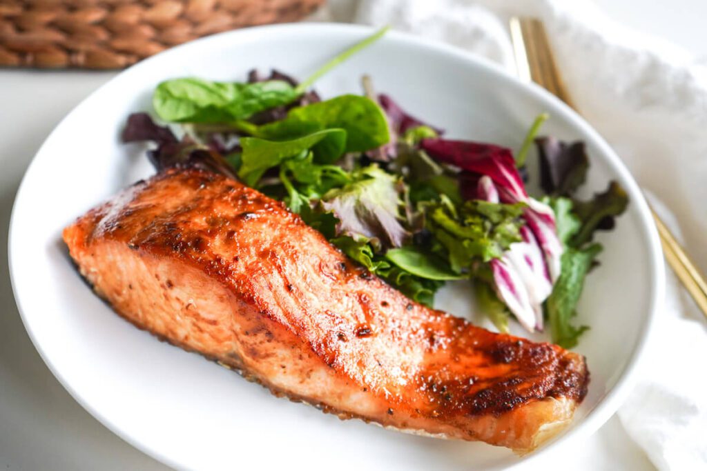 Close up shot of flaky air fryer maple balsamic salmon served with fresh salad greens.