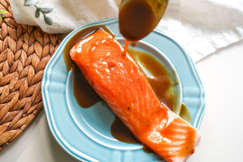 Pouring homemade maple balsamic glaze over a fresh raw salmon fillet on a blue plate.